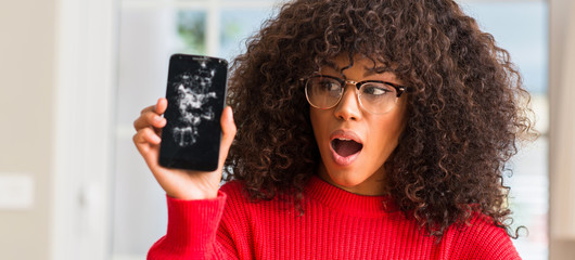 Sticker - African american woman holding broken smartphone scared in shock with a surprise face, afraid and excited with fear expression