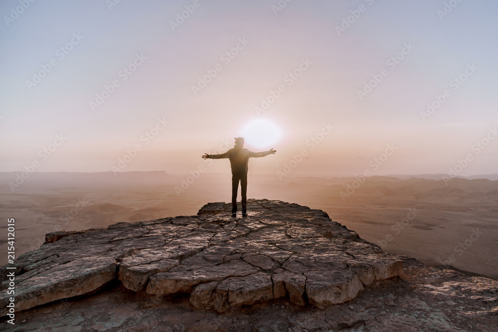 Alone man in israel negev desert admires the view of sunrise. Young male person stands on the edge of the cliff - obrazy, fototapety, plakaty 