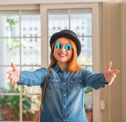 Sticker - Stylish redhead woman wearing bowler hat and sunglasses looking at the camera smiling with open arms for hug. Cheerful expression embracing happiness.