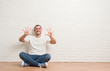 © Krakenimages.com - Young caucasian man sitting on the floor over white brick wall showing and pointing up with fingers number ten while smiling confident and happy.