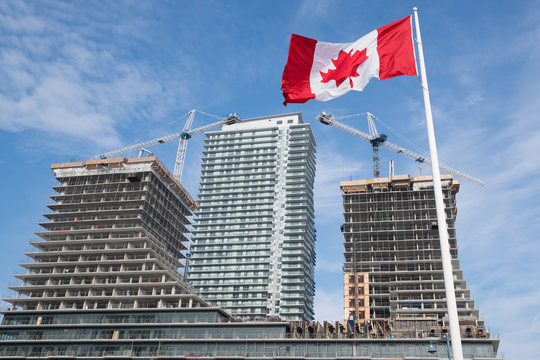Canadian flag and cranes on construction site in Toronto, Canada