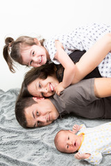 Wall Mural - Happy family of four looking at the camera on their bed with child and newborn baby