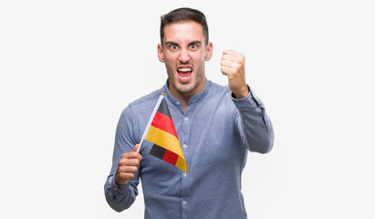 Canvas Print - Handsome young man holding a flag of Germany annoyed and frustrated shouting with anger, crazy and yelling with raised hand, anger concept