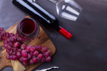 Wall Mural - Bottle of red wine and two wine glasses - oned filed and empty one, on table with grape, banner