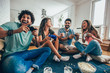 © Mediteraneo - Group of friends play video games together at home, having fun.
