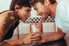 Romantic Couple Sharing Milk Shake Using Straws From The Same Gl