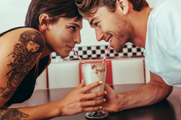 Romantic couple sharing milk shake using straws from the same gl