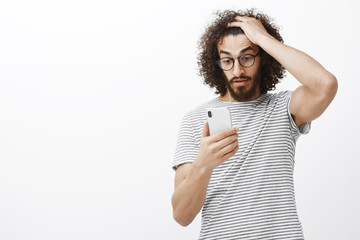 Wall Mural - No way, cannot handle this pressure. Frustrated confused male with beard, touching curly hair and staring at smartphone stunned, being shocked with amazing unexpected message, standing upset