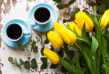 two blue cup of coffee with yellow tulips on an old table