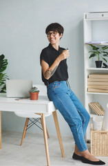 Young woman with cup of coffee standing near the table in the office