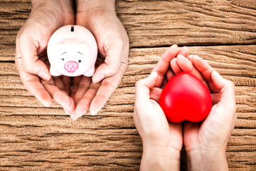 Wall Mural - Man and women hand hold a piggy bank and red heart with copy space on old wood background, Health insurance concept.