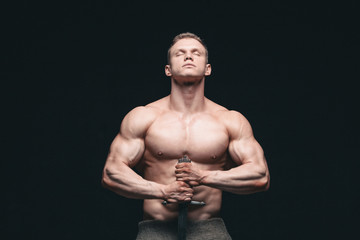 Wall Mural - Bodybuilder man posing with a sword isolated on black background. Serious shirtless man demonstrating his mascular body. hands on a sword