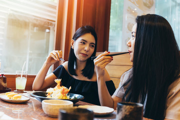 Two young attractive Asian women eating Shrimp Tempura Japanese food at restaurant with happiness and joy