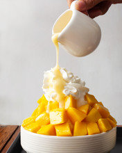 Shaved Ice Dessert. Woman Hand Pouring Sweetened Condensed Milk On Whipped Cream. Served With Mango Sliced And Vanilla Ice Cream.
