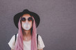 Young hipster woman with long pink hair blowing a bubble with bubble gum.