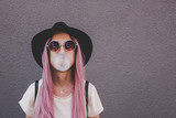 Fototapeta  - Young hipster woman with long pink hair blowing a bubble with bubble gum.