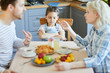 © pressmaster - Upset little girl sitting by served table while her parents having quarrel at breakfast