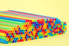 Hundreds Of Colorful Plastic Straws Laying On Yellow Surface With Yellow Background Facing Open End At An Angle Towards Viewer. Many Cities Are Now Banning Single Use Plastic Straws.