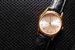 Women's wristwatch. Gold metal watch. Black fabric background pattern. Clock hands. Black leather strap. Time.
