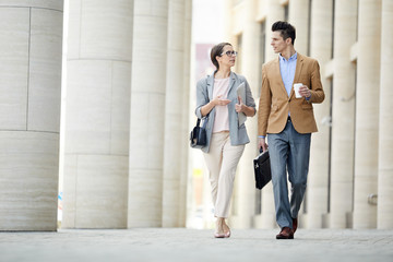 Two young colleagues in formalwear having talk while going back home from work