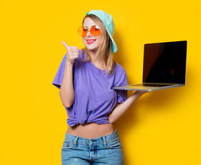 Wall Mural - Young style girl with orange glasses and laptop computer on yellow background. Clothes in 1980s style