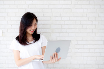 Wall Mural - Beautiful of portrait young asian woman smiling and standing holding laptop on brick cement wall background, girl working computer, business and lifestyle concept.