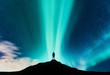 © den-belitsky - Aurora borealis and silhouette of standing man on the mountain. Aurora and traveller. Starry sky and green polar lights. Night landscape with northern lights and people. Concept. Nature background