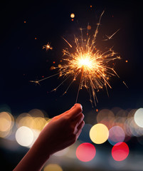 Wall Mural - Hand holding a sparkler with blurred busy city light