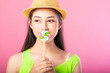 © Sasils Production - Portrait of a smiling attractive woman in summer outfit and hat posing with lollipop over her mouth and looking at camera isolated over pink background.