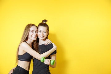 Portrait of two fitness females on yellow background. Young women friends standing against wall and smiling