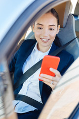 Wall Mural - Successful businesswoman. Happy pleasant woman using her gadget while riding in the car