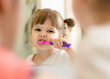 © Oksana Kuzmina - Cute little child girl brushing teeth and looking in mirror in bathroom