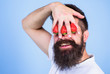 Dream of strawberry. Man bearded hipster hold hand with strawberries in front of eyes. Strawberry on my mind. Man can not see anything but strawberry blue background. Glance of man blocked by berries