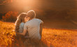 canvas print picture - Stylish young couple sitting on a hill and admiring the sunset. A film photo with a light and a sunlight, a foreshortening from the back. Enamored youth in the second before the kiss