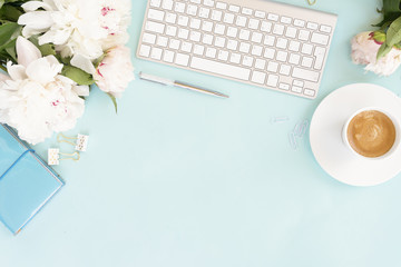 Flat lay home office workspace background with white modern keyboard, notebook and peony flowers, copy space on blue background