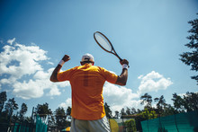 Male Flourishing Hands With Sport Equipment While Turning Back To Camera. He Winning During Game While Locating Under Blue Sky