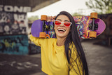 Fototapeta  - Sexy slim fit brunette woman in sport casual outfit in a skate park. Active leisure on a longboard