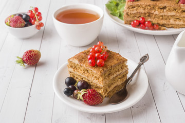 Honey cake with strawberries, mint and currant, a Cup of tea on a light background.