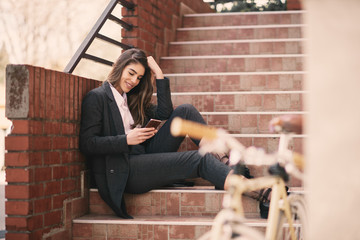 Wall Mural - Portrait of woman using smart phone while sitting on stairs outdoors.