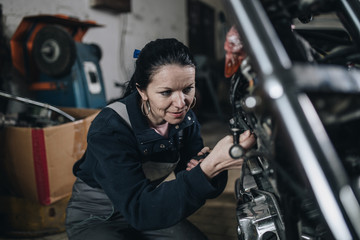 Wall Mural - Strong and worthy woman doing hard job in car and motorcycle repair shop.