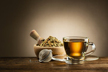 Glass Cup Of Tea With Infuser And Herbal Tea On Wooden Table
