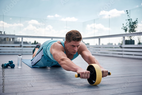 Fotografía Concentrated young guy is exercising with sport equipment on roof of urban building