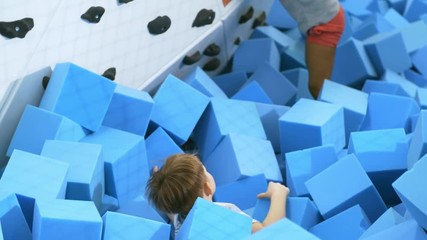 Wall Mural - High angle view of little boy having fun in cube pit and throwing blue soft foam cubes at his female friend