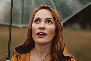 Wall Mural - Waist up portrait of amazed woman looking upwards with open mouth. She is holding umbrella and gazing at sky waiting for rain