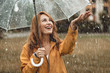 © Yakobchuk Olena - Waist up portrait of cheerful girl holding umbrella and catching rain drops with smile. She is stretching hand and looking upwards with sincere delight