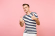 Portrait of businesslike young man in striped t-shirt showing thumbs up gesture on copy space isolated on trending pastel pink background. People sincere emotions lifestyle concept. Advertising area.