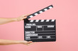 Close up female holding in hand classic director clear empty black film making clapperboard isolated on trending pastel pink background. Cinematography production concept. Copy space for advertising.