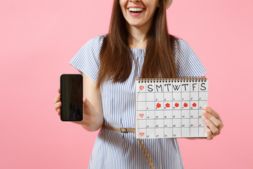 Woman holding female periods calendar for checking menstruation days, mobile phone with blank black empty screen isolated on pink background. Medical, healthcare, gynecological concept. Copy space.
