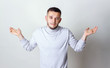 I don't know concept. Portrait of a young man who do not understand what is happening. Man in white turtleneck raises hands and shrugging his shoulders on a gray background copy space