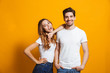 © Drobot Dean - Photo of beautiful couple man and woman in basic clothing standing together and smiling at camera, isolated over yellow background